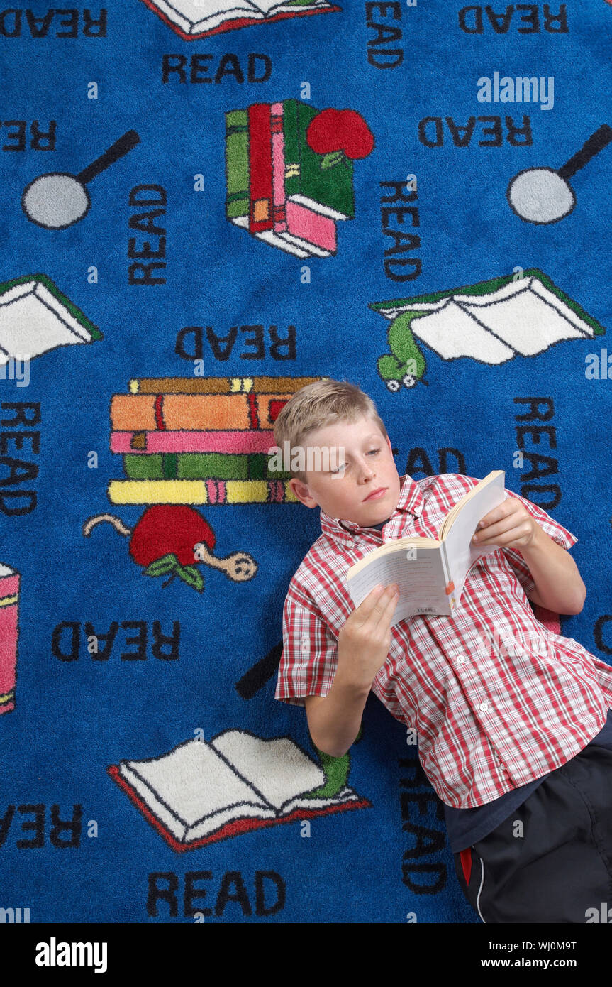 School boy reading book on floor in library Stock Photo - Alamy