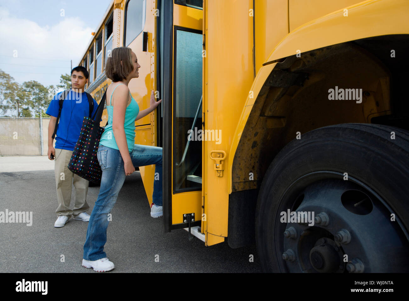 Young female student getting on school bus with classmate standing by it Stock Photo