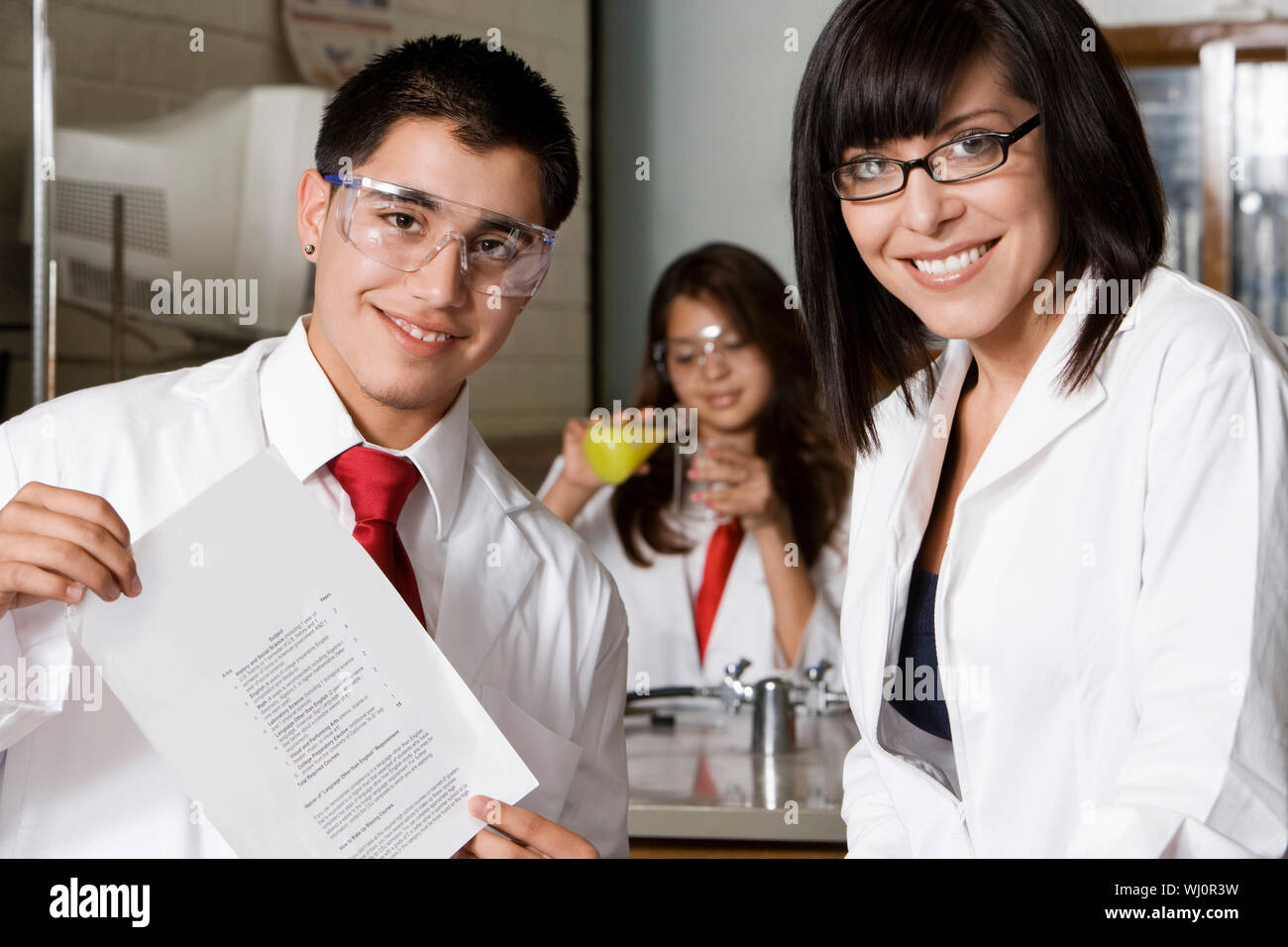 Portrait of professor and male student holding report with classmate experimenting in the background Stock Photo