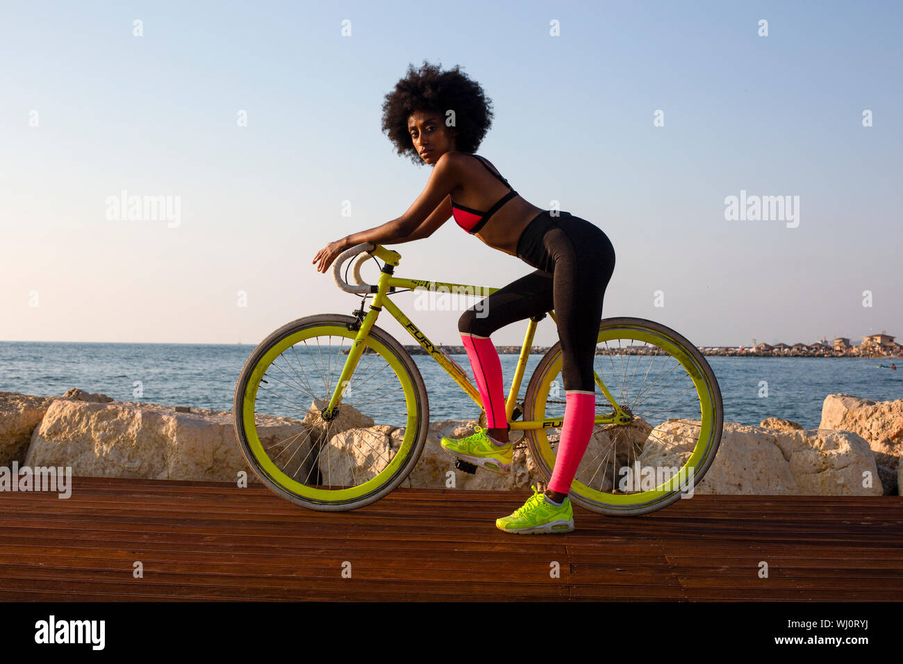 Young athletic woman in sports clothes with her road bicycle near the sea Stock Photo