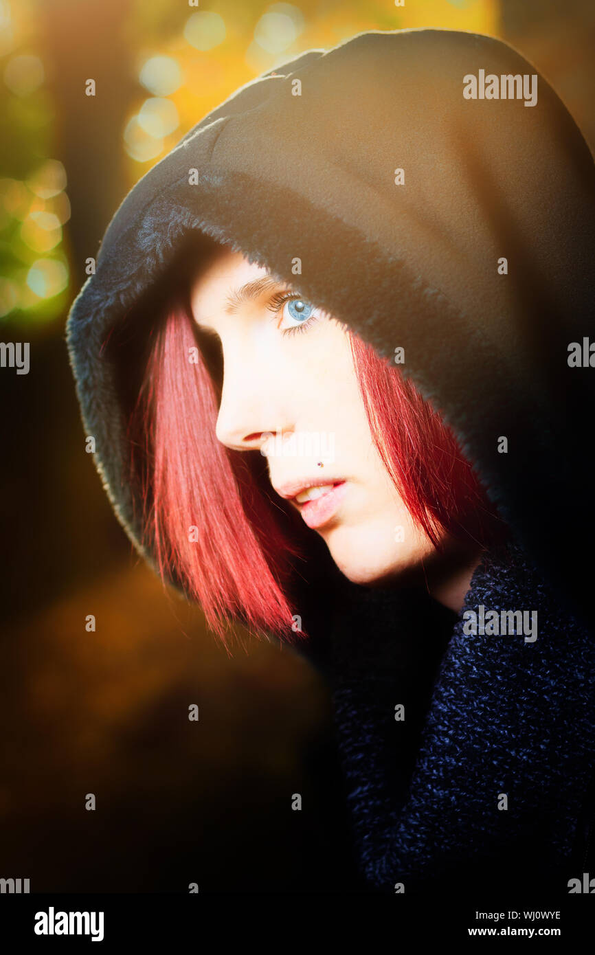 Head and shoulders portrait of a beautiful redhead woman with blue eyes standing in profile outdoors wearing a hooded anorak Stock Photo