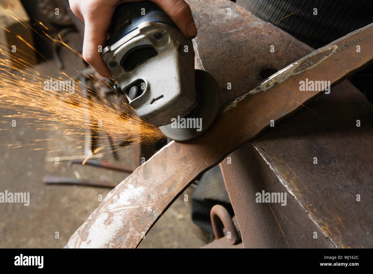 Blacksmith using angle grinder on edge of metal tool in workshop Stock Photo