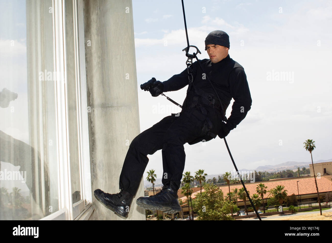 Full length of a armed man hanging on rope and aiming the target ...
