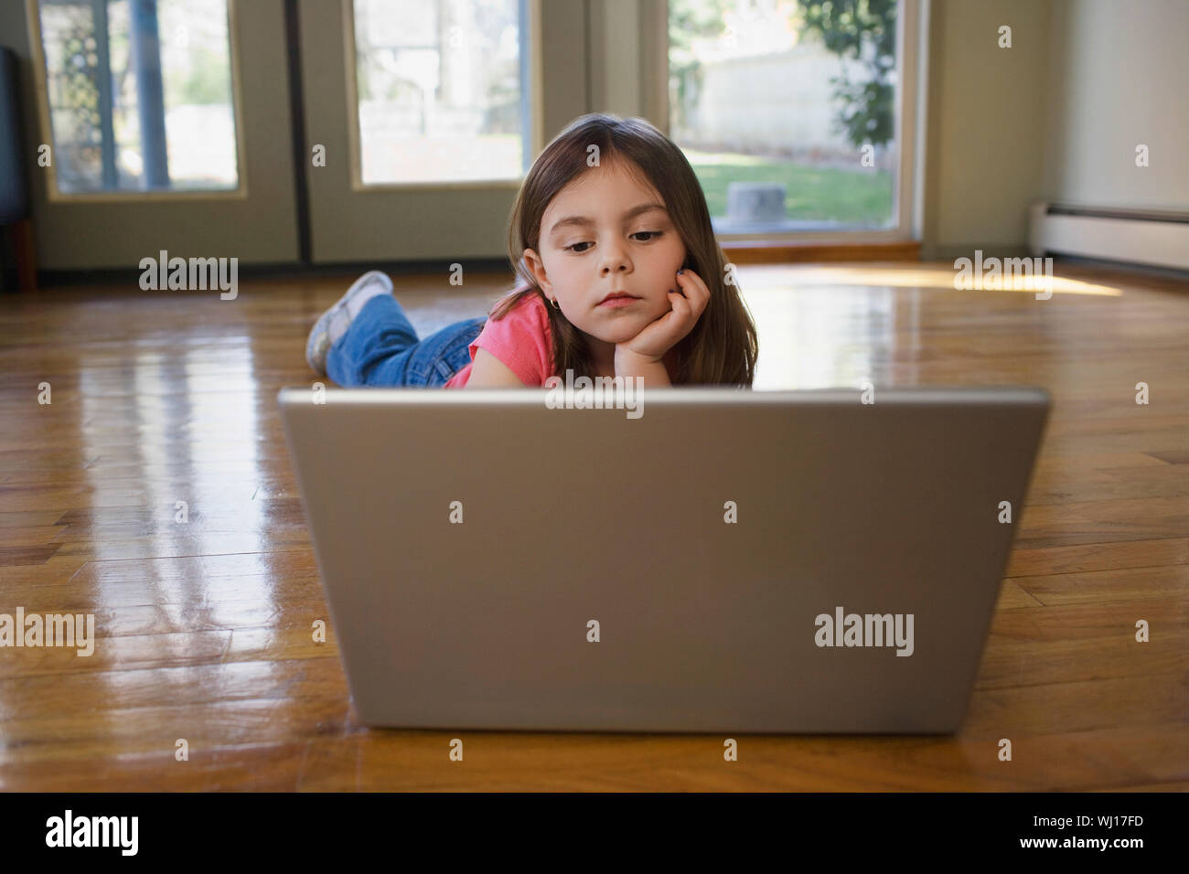 Serious young girl using laptop while lying on hardwood floor Stock ...