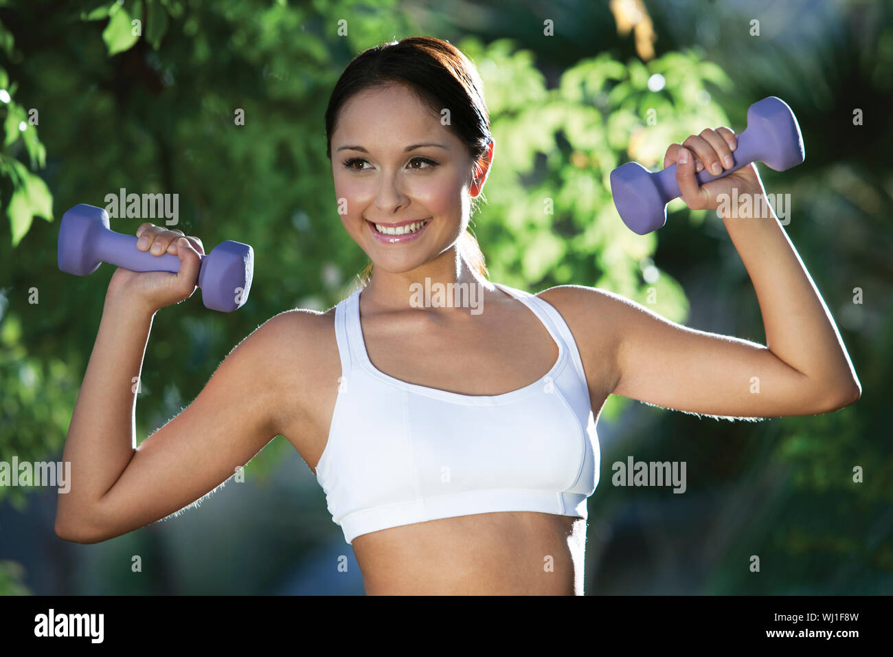 Smiling young woman exercising with dumbbells in the park Stock Photo