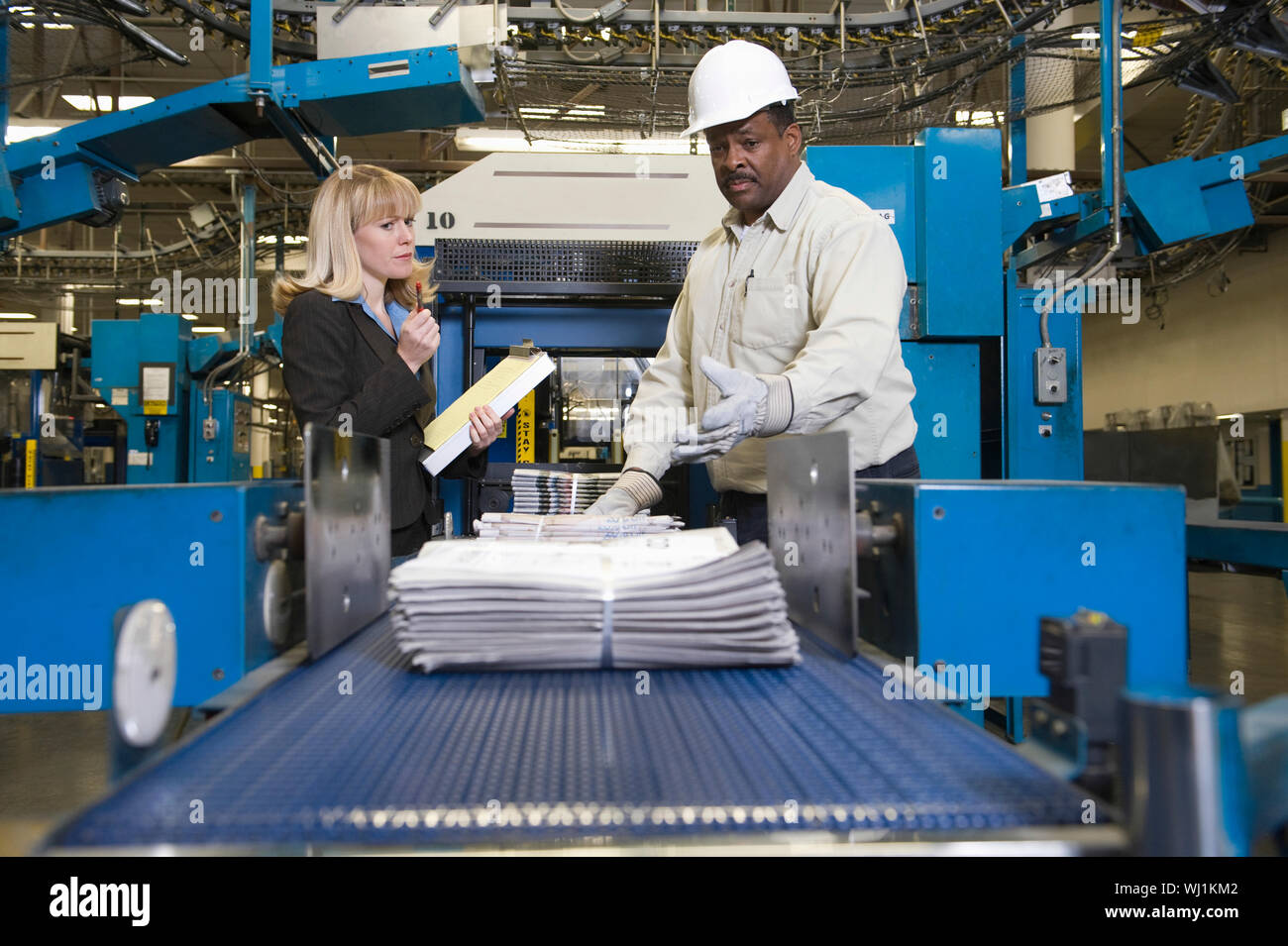 Side view of a woman by man working on newspaper production line in