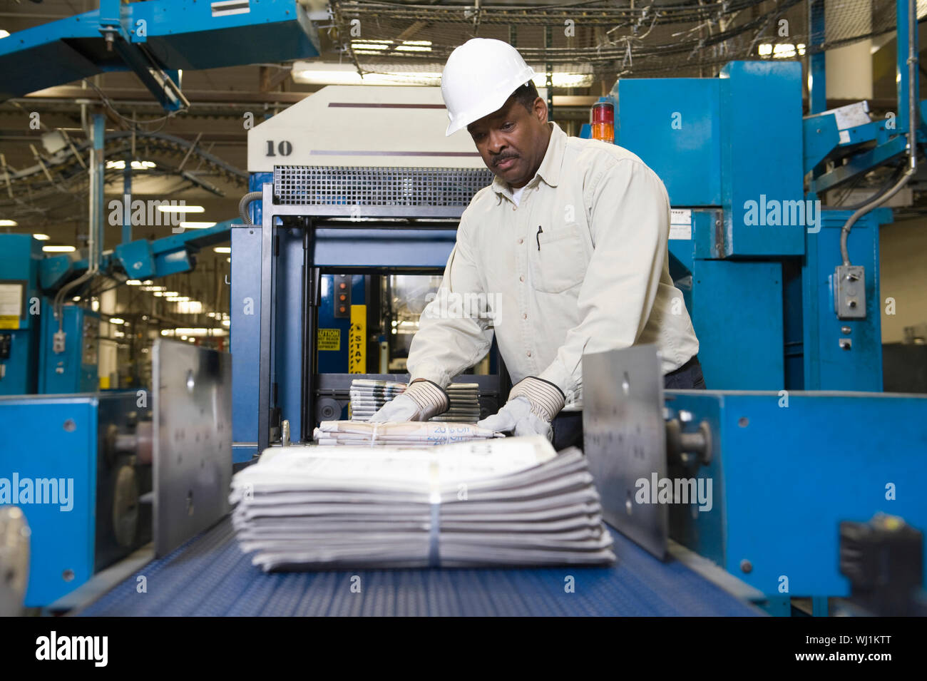 Side view of a man working on newspaper production line in newspaper