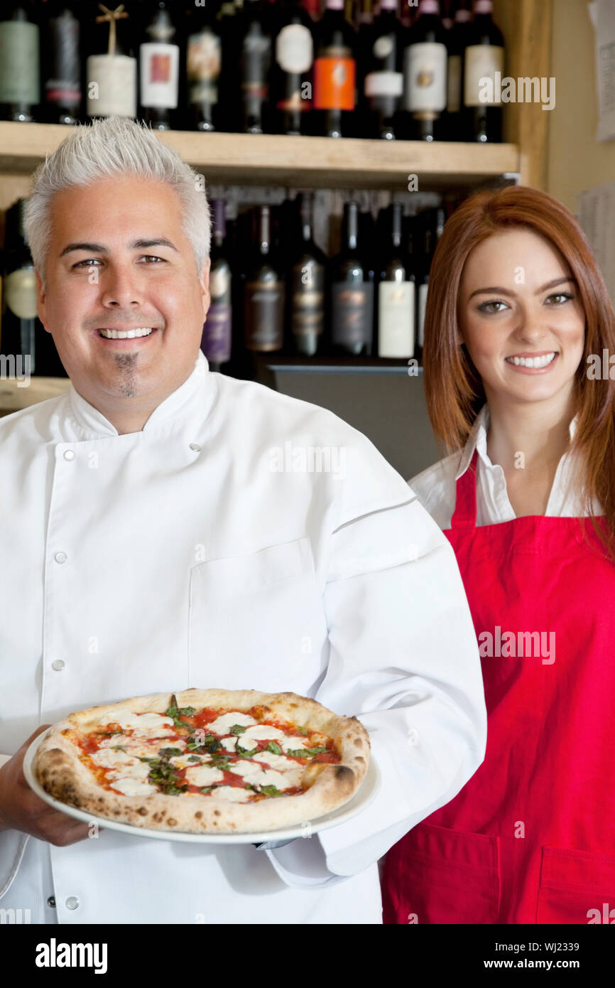 Portrait of a happy chef holding pizza with beautiful waitress Stock Photo