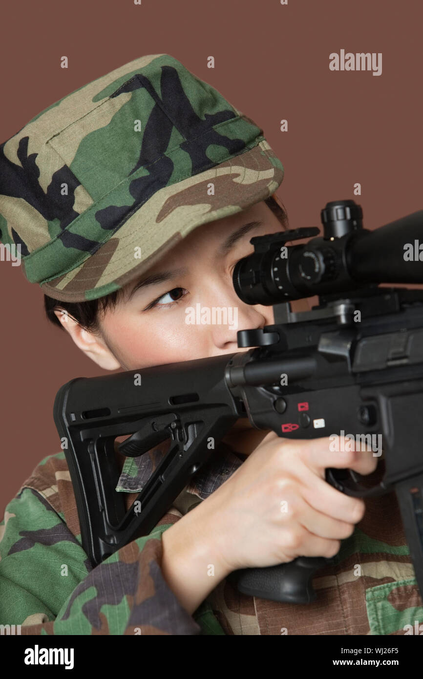 Young female Marine Corps soldier aiming M4 assault rifle over brown background Stock Photo