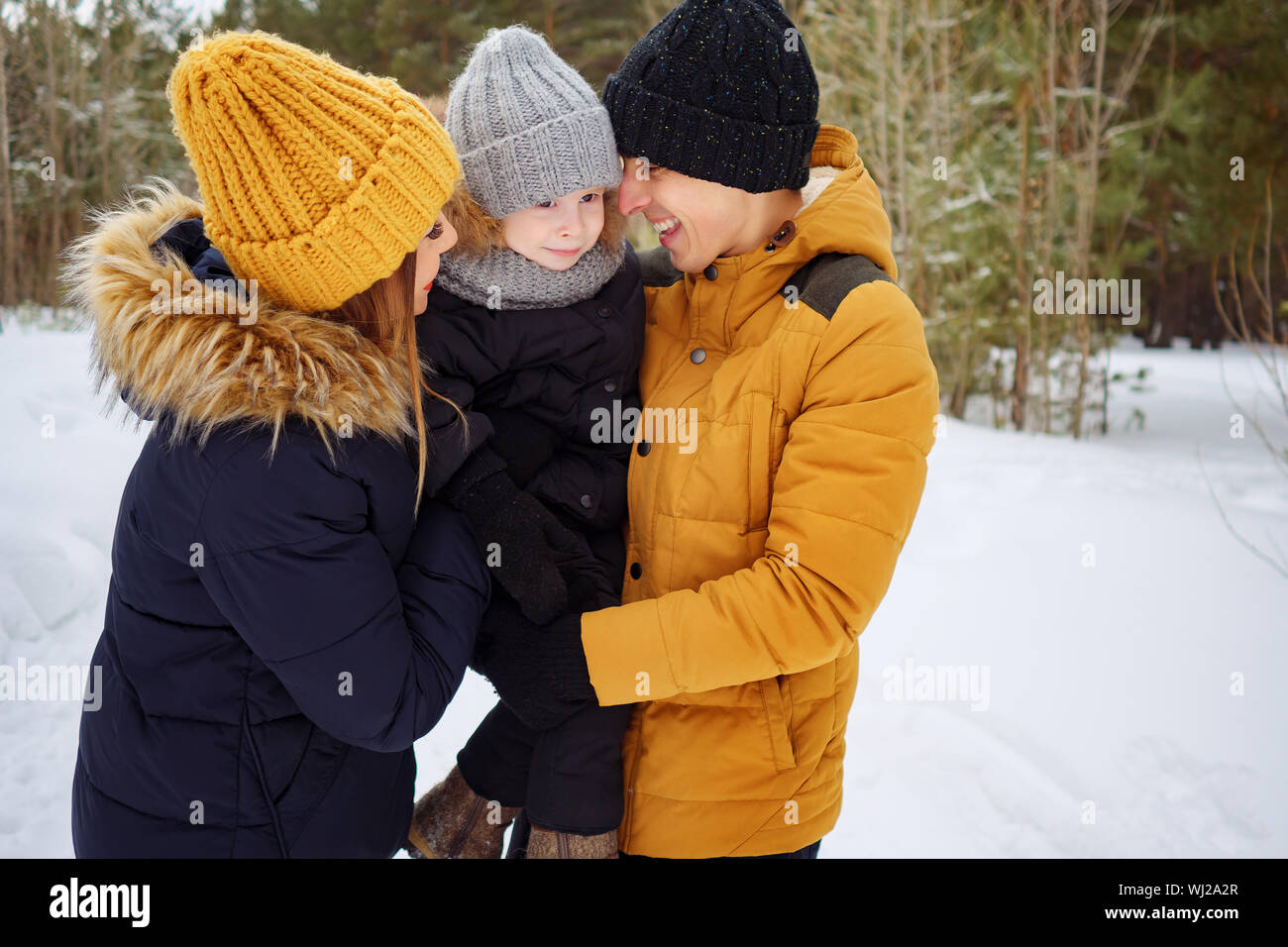 Portrait of happy family in winter day. Mom and dad are cuddling their little son in winter park. Family lovely moments. Stock Photo