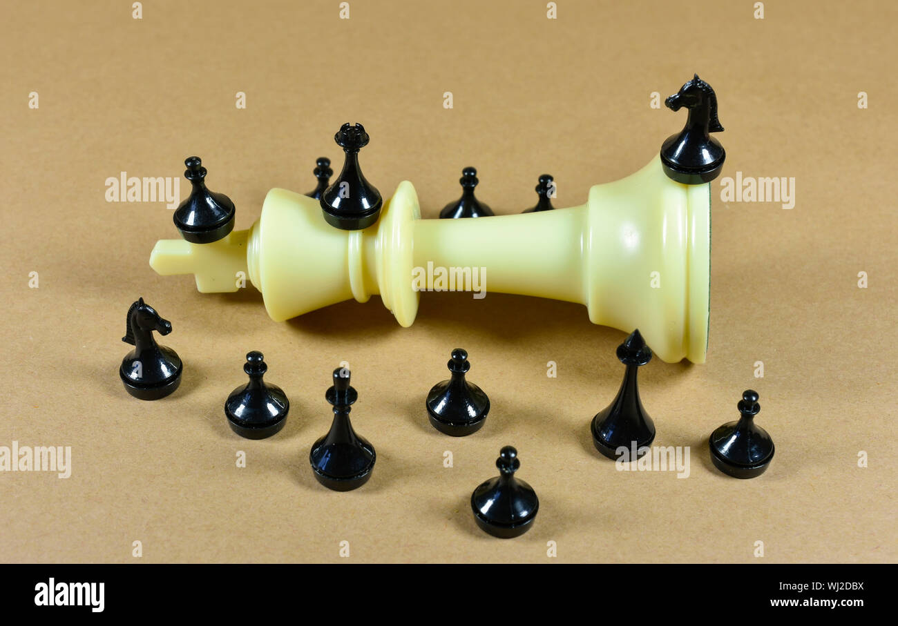 White king chess piece fallen on a board with black small chess pieces surrounding it, conceptual image about leadership , competition and business Stock Photo