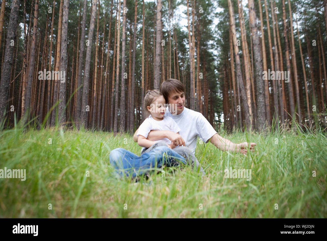 Happy father and daughter sitting on grass in forest Stock Photo - Alamy