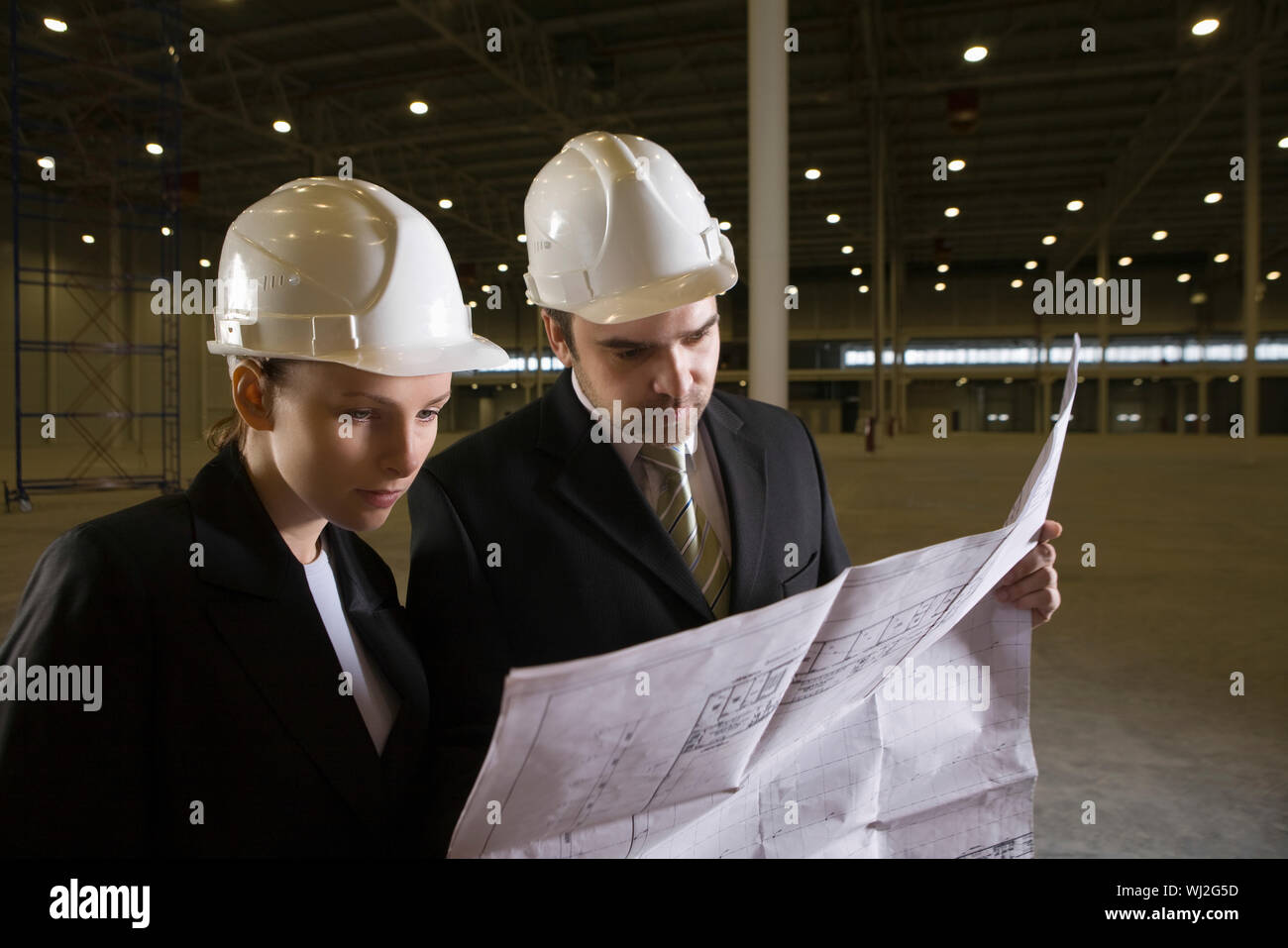 Two young architects looking at blueprint in empty warehouse Stock Photo