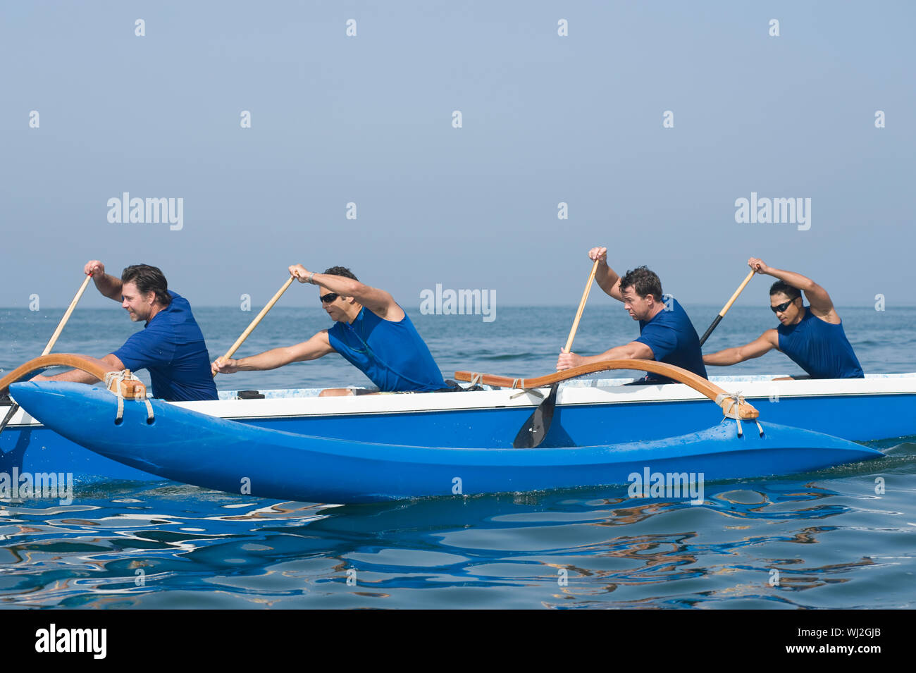 Side view of male rowers paddling outrigger canoe in race Stock Photo