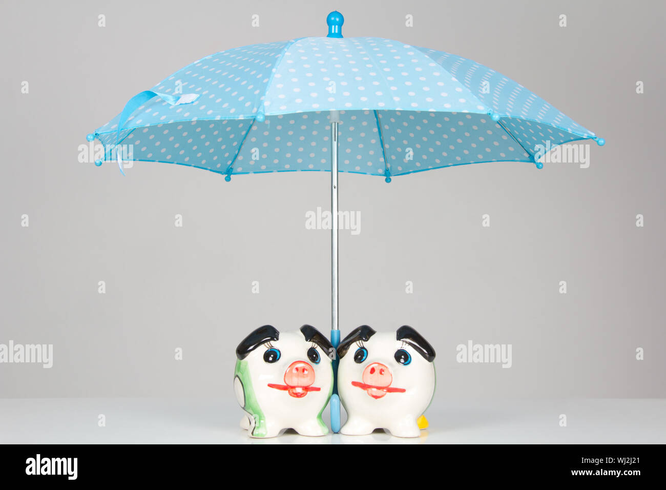 Two piggy banks under an umbrella on table Stock Photo - Alamy