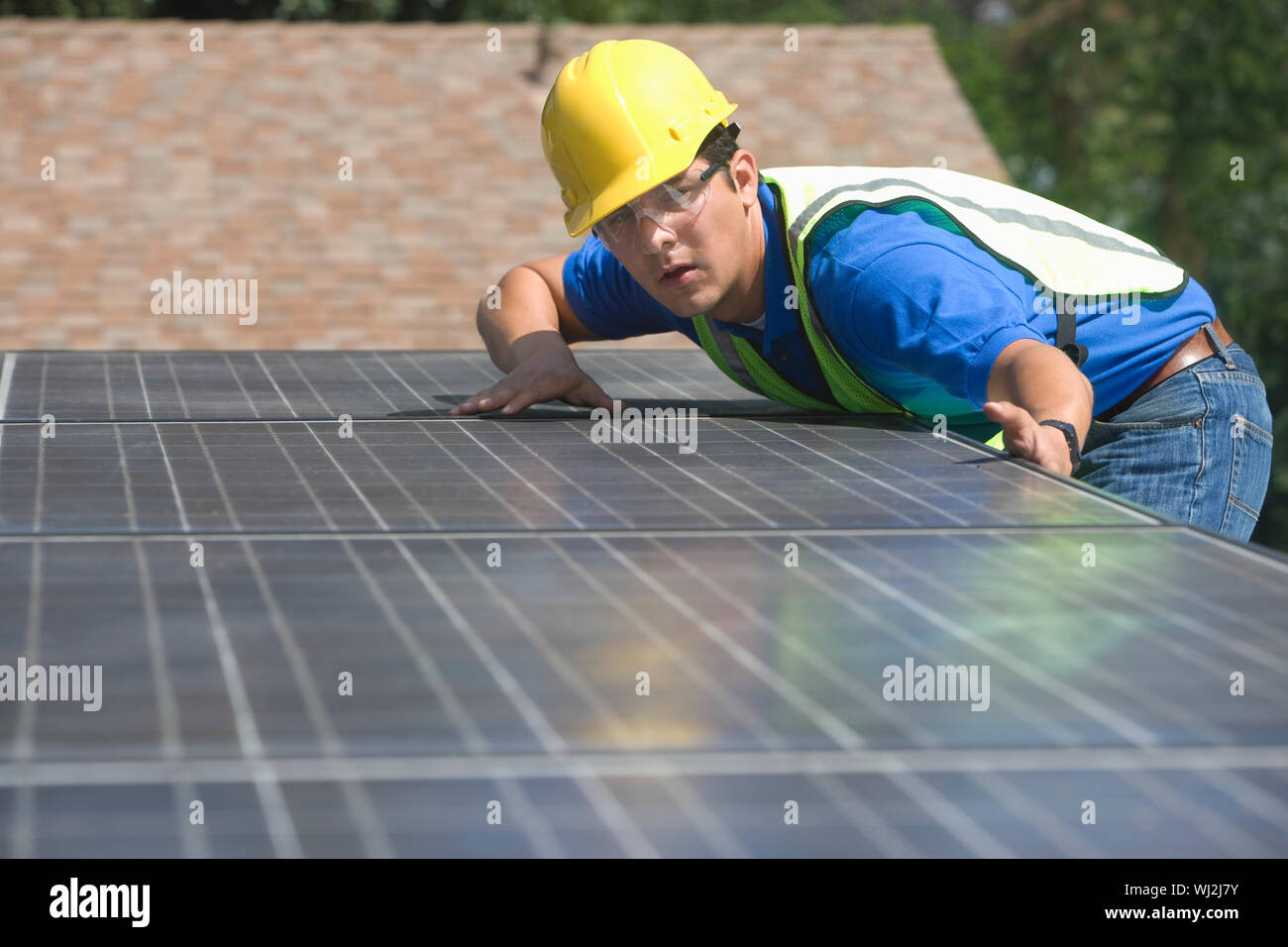 Young maintenance worker installing solar panels on rooftop Stock Photo