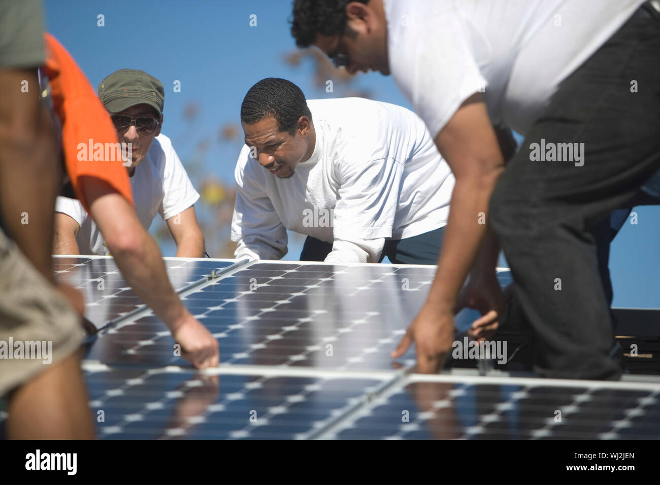 Group of multiethnic engineers placing solar panel on rooftop Stock Photo