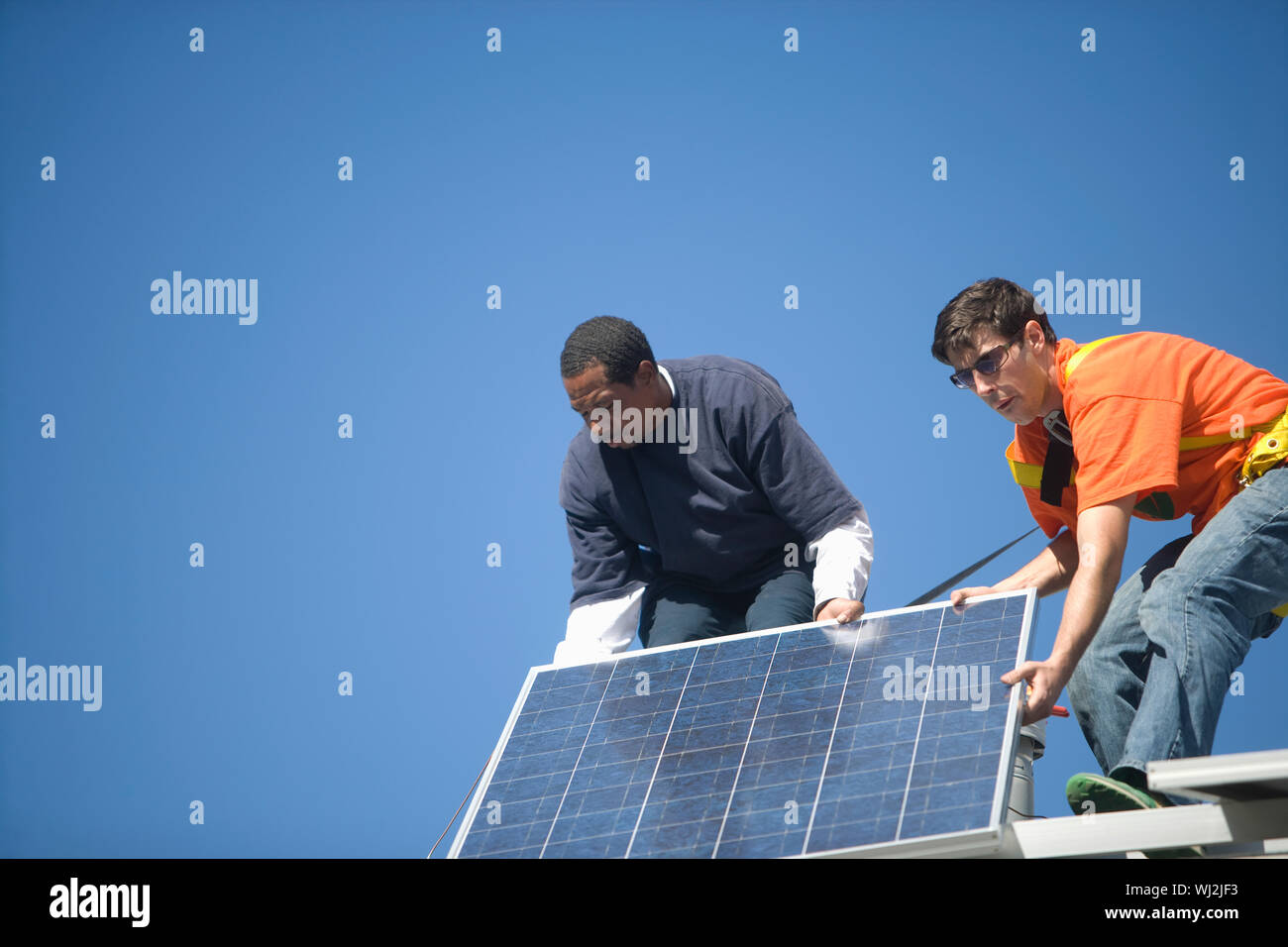 Low angle view of engineers fixing solar panel against blue sky Stock Photo