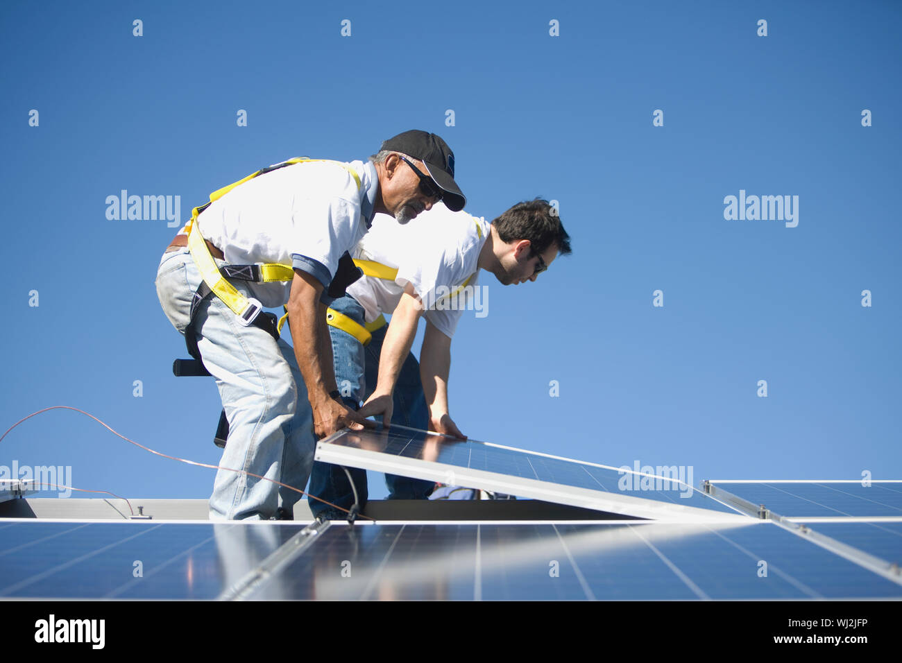 Side view of multiethnic engineers placing solar panel against blue sky Stock Photo