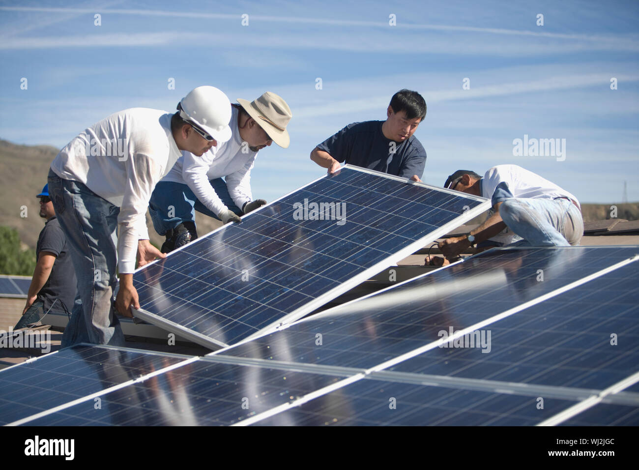 Group of multietchinc engineers placing solar panels on rooftop Stock Photo