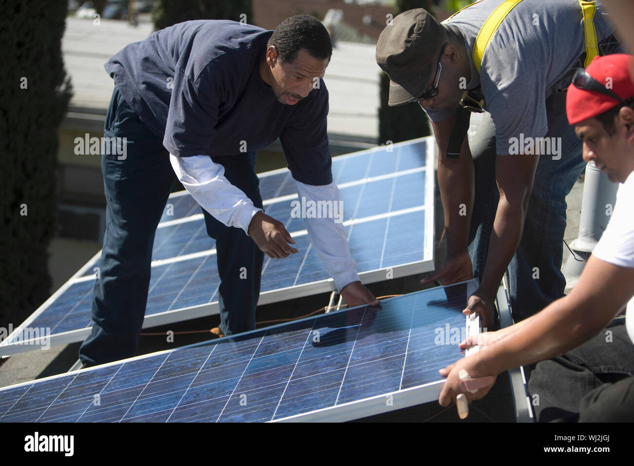 Multietchinc engineers placing solar panel together on rooftop Stock Photo