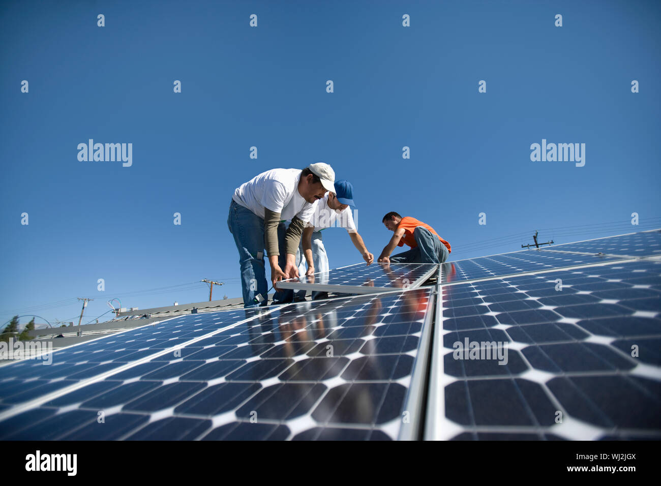 Interracial engineers placing solar panel against clear blue sky Stock Photo