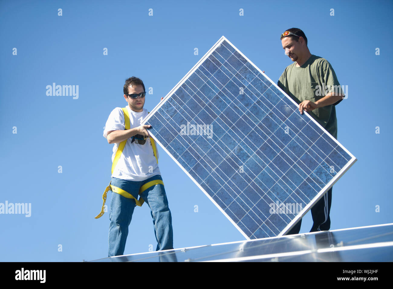 Young interracial engineers holding solar panel againat blue sky Stock Photo