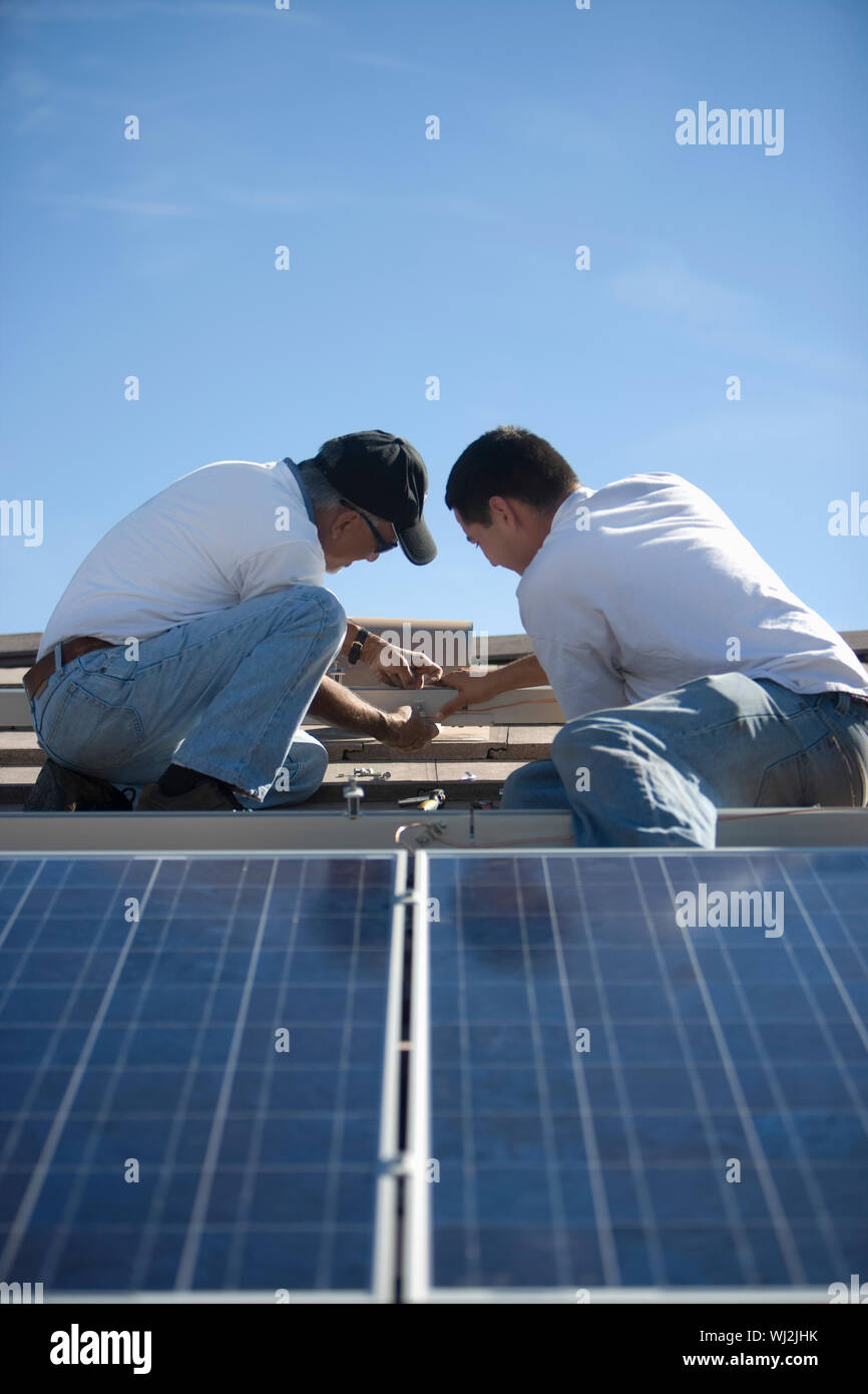 Two engineers working on solar panelling at rooftop against blue sky Stock Photo