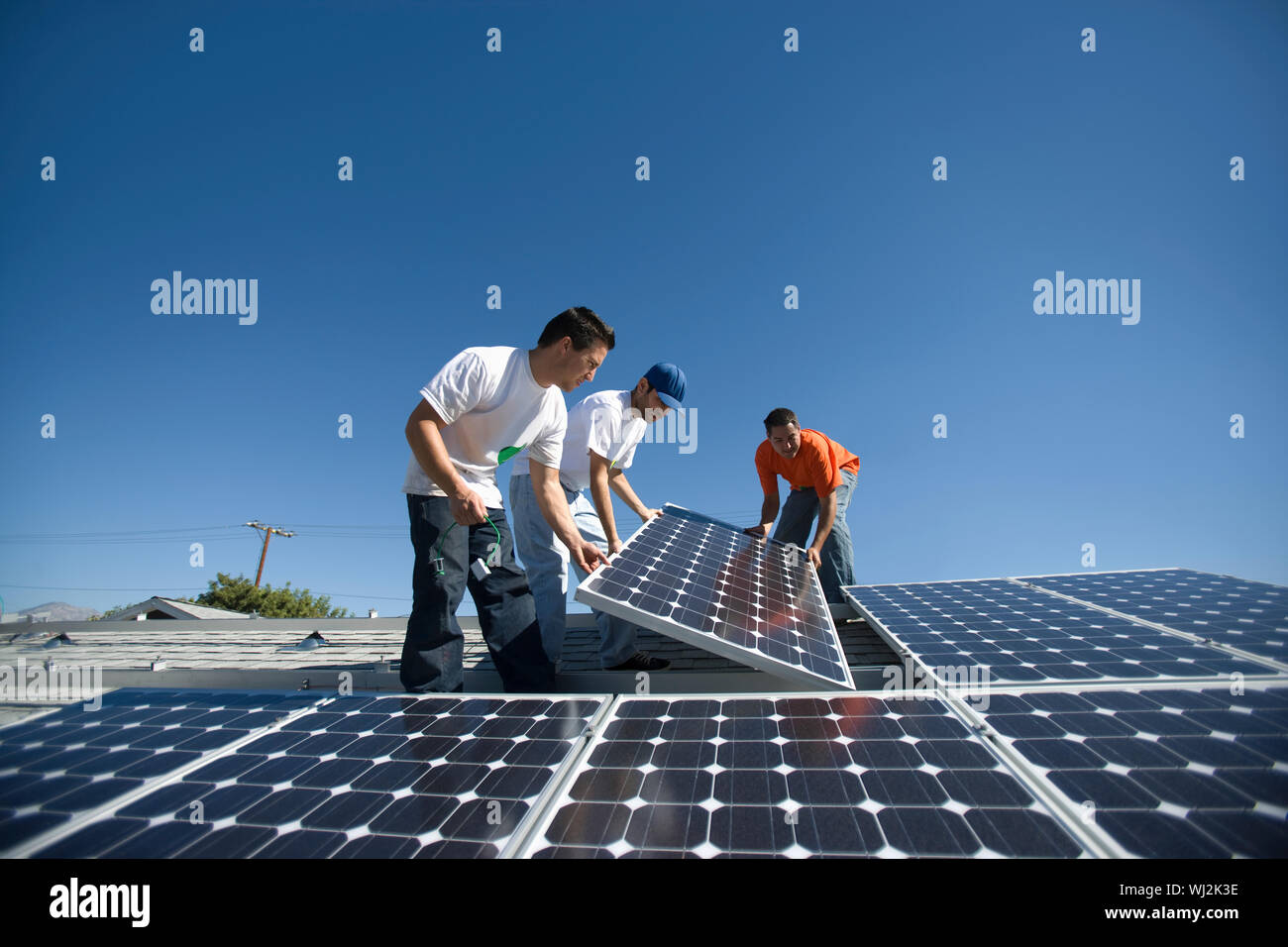 Interracial engineers positioning solar panel against clear blue sky Stock Photo