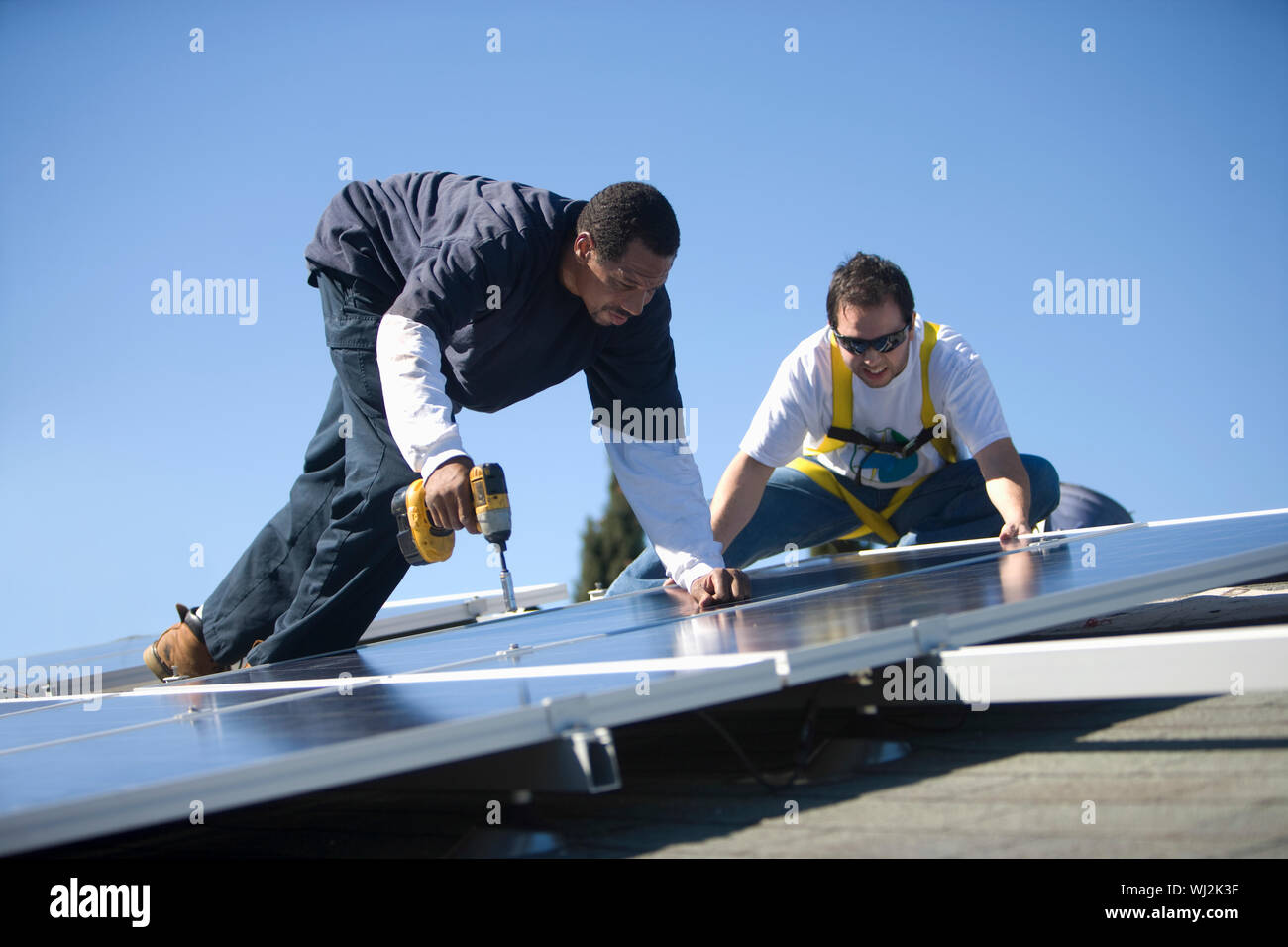 Two engineers working on solar panels against blue sky Stock Photo