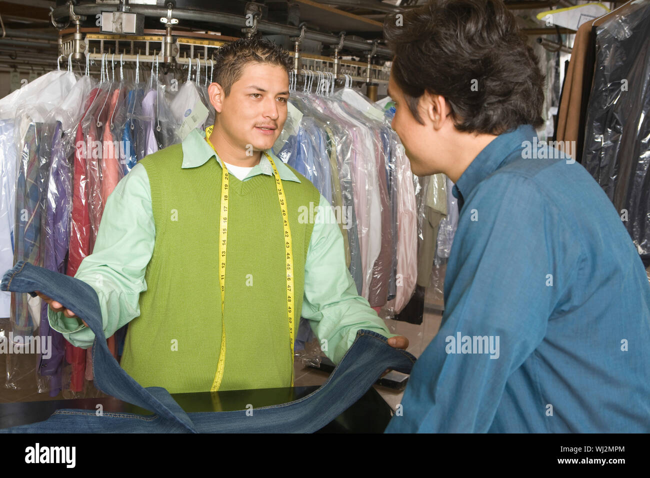 Young male owner showing dry cleaned jeans to customer at counter in