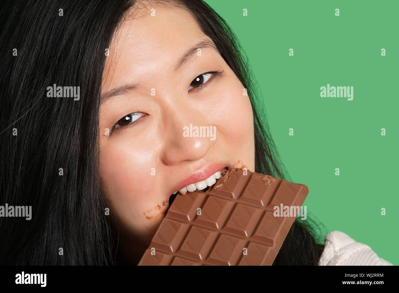 portrait of a young woman eating chocolate over green background. 