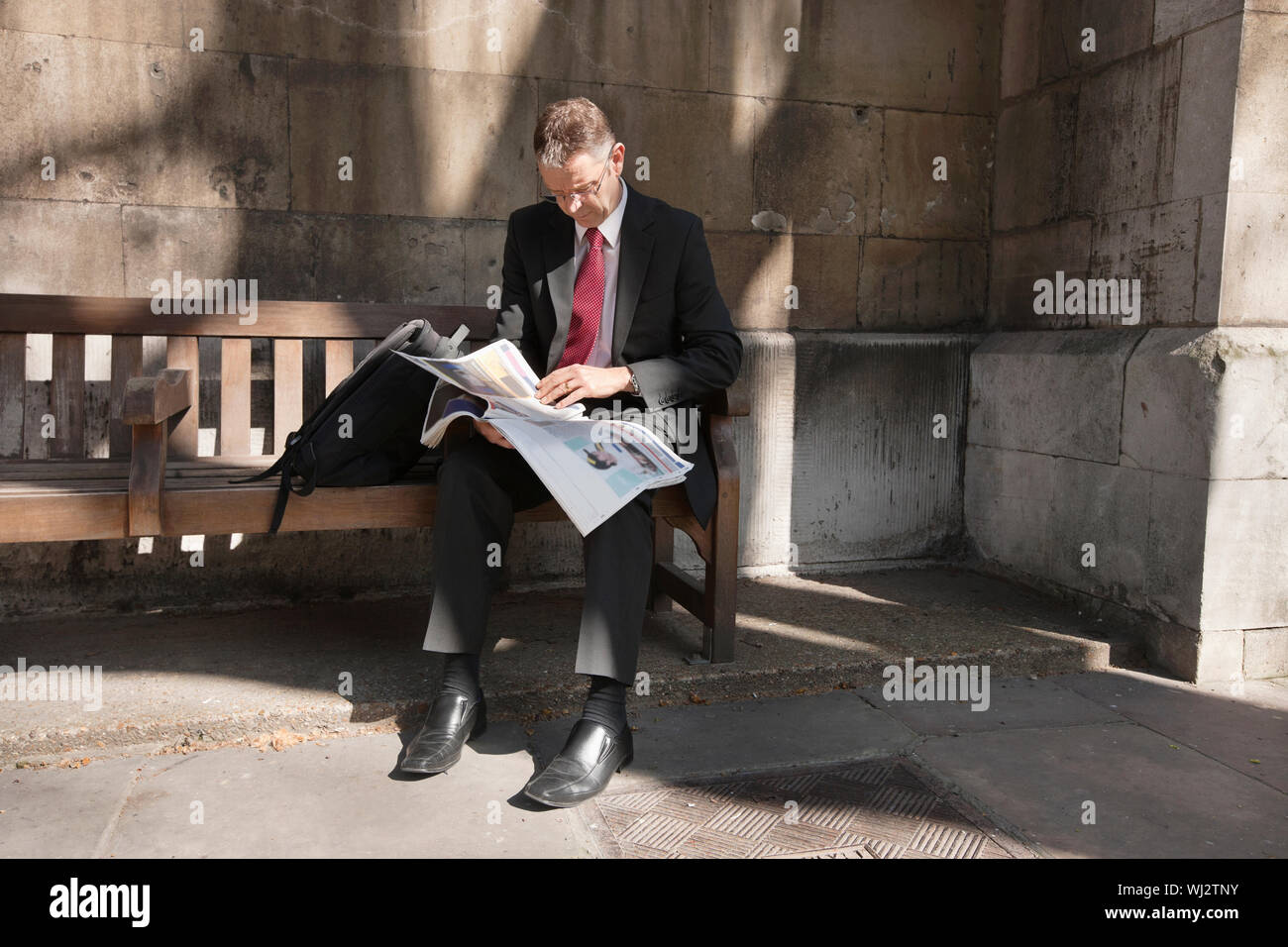 Mature businessman sitting on bench reading newspaper Stock Photo - Alamy