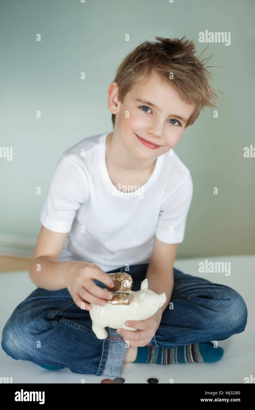 Portrait of young boy putting coin in piggy bank Stock Photo - Alamy