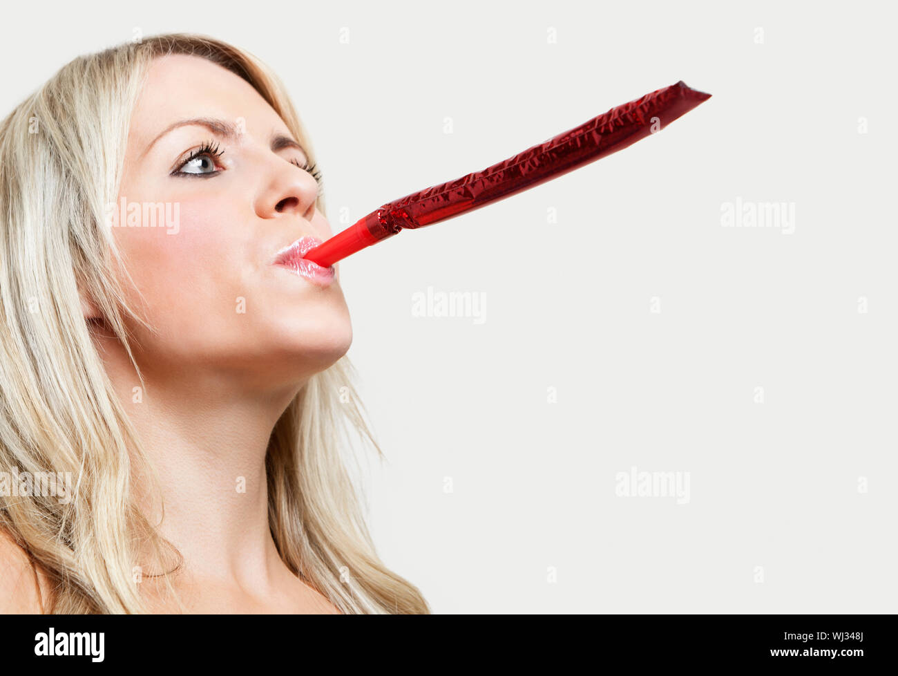 Close-up of a young woman blowing party blower against gray background ...