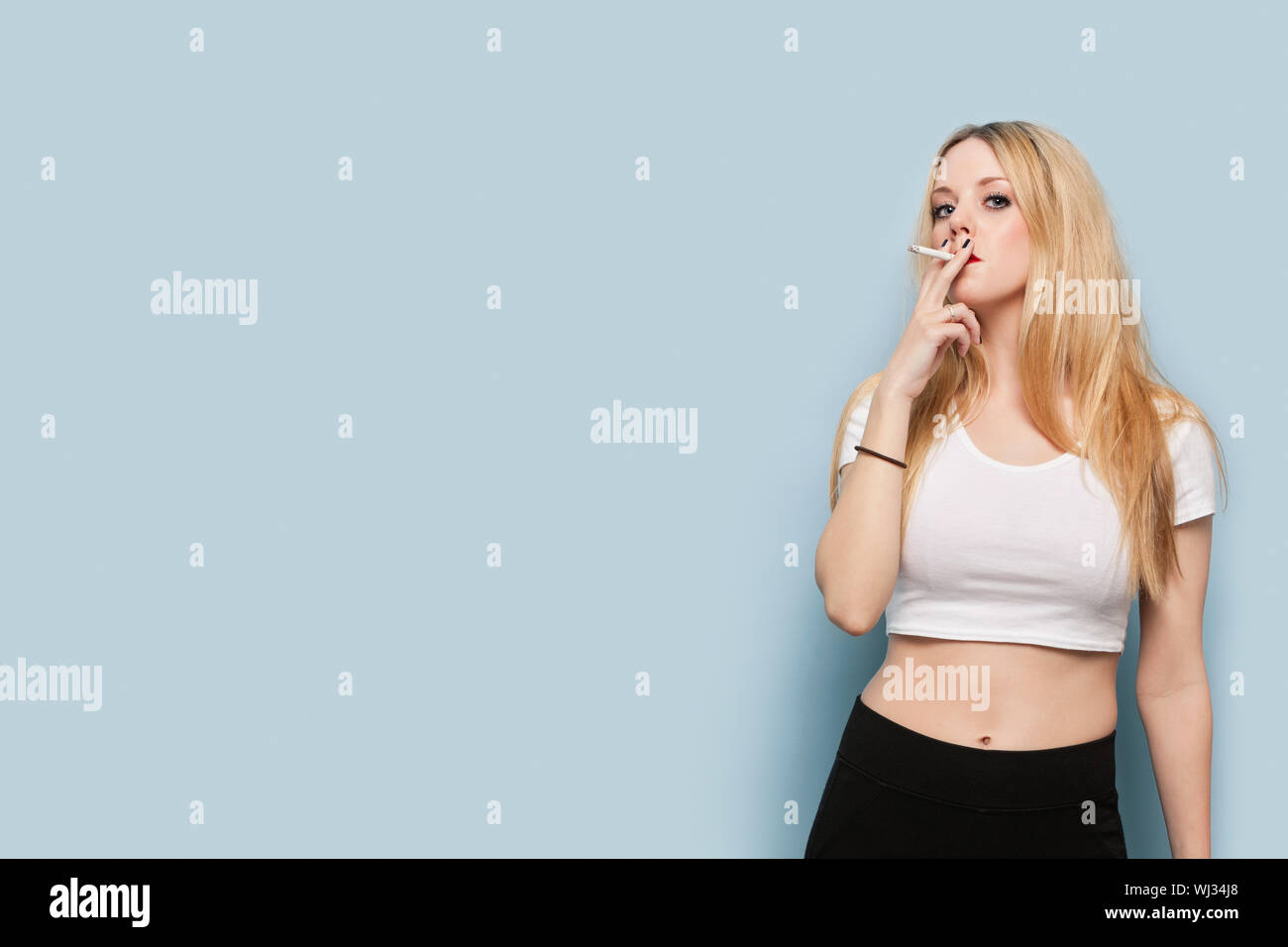 Portrait Of Young Woman Smoking Cigarette Against Light Blue