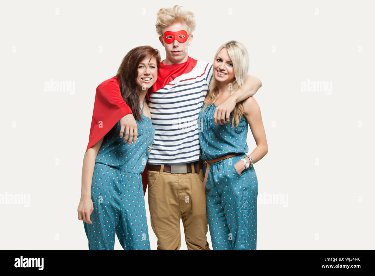 Portrait of young man in superhero costume and women wearing jumpsuits standing together against gray background Stock Photo