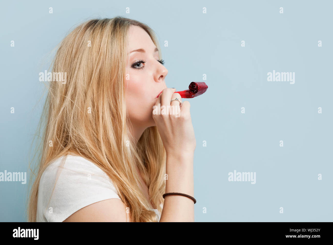 Young woman with party blower against light blue background Stock Photo ...