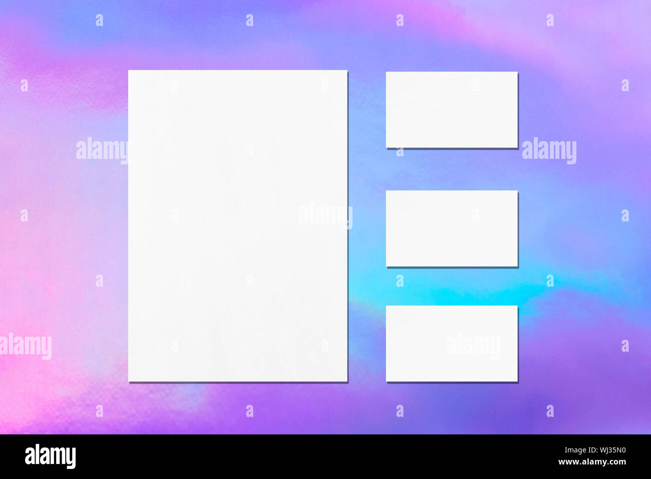 One empty white vertical a4 sized poster and three horizontal rectangle business card mockups with soft shadows on holographic background. Flat lay, t Stock Photo