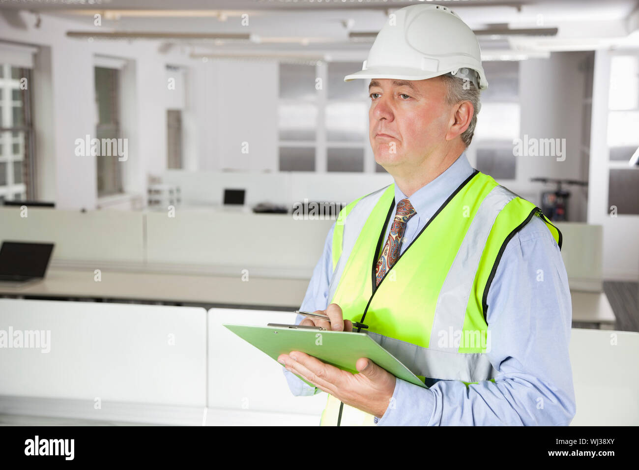 Office Reflator Middle-aged man in reflector vest and hard hat with clipboard at office ...