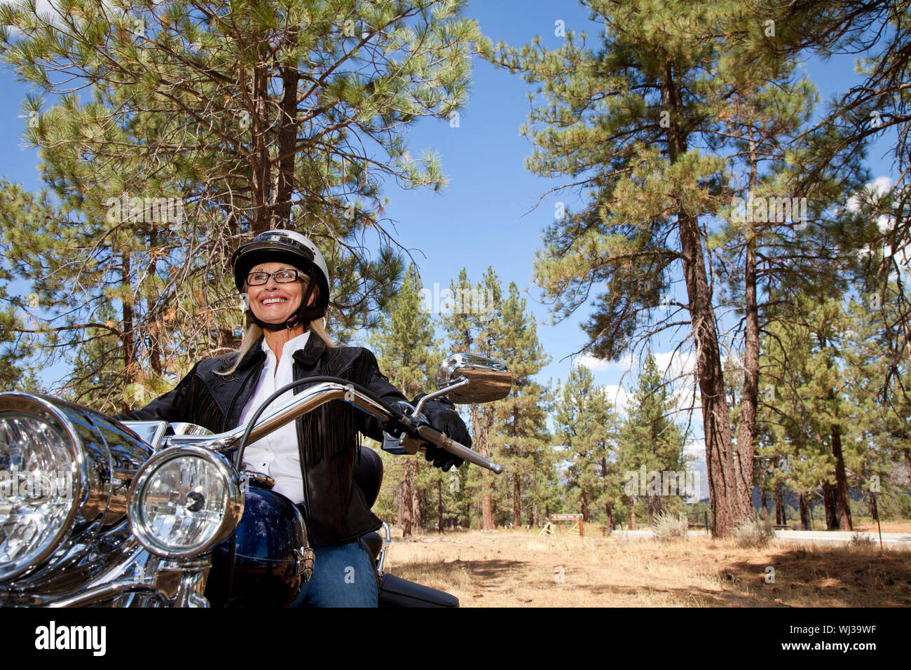 Senior woman riding motorcycle through a forest Stock Photo