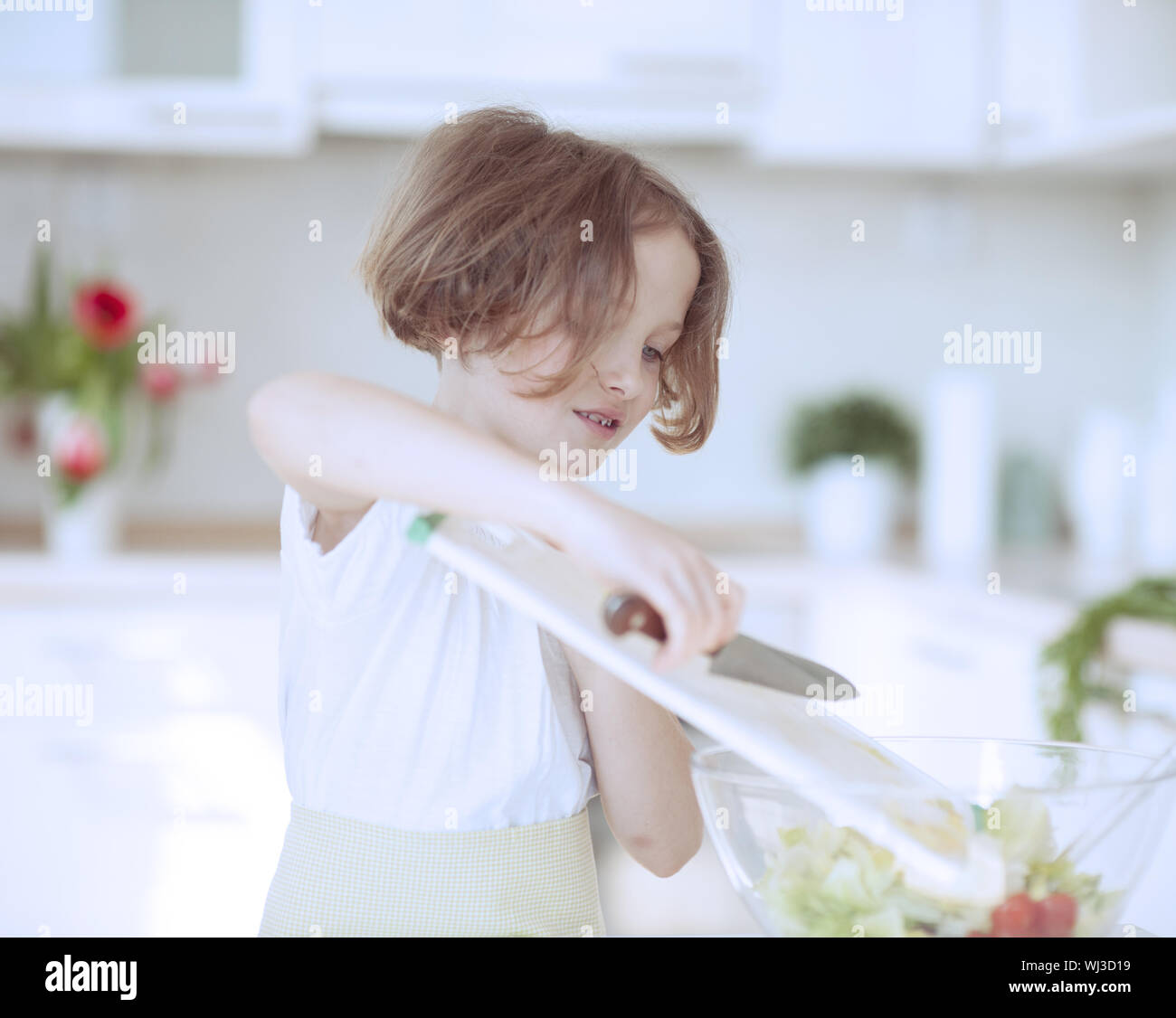 Young girl placing lettuce in salad bowl using a knife Stock Photo