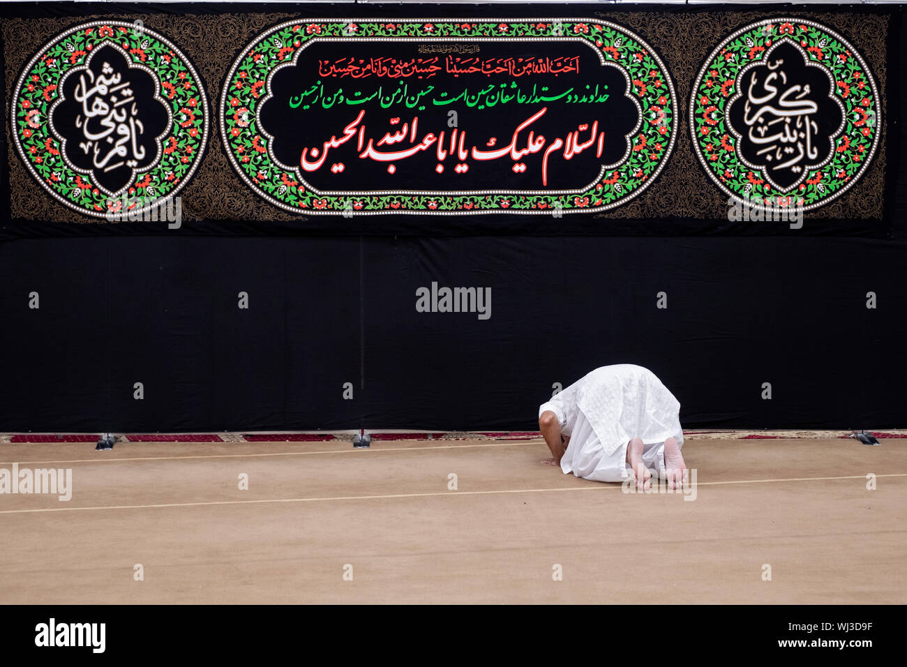 A devout Muslim man bows in prayer in front of Koran quotes at the Imam Al-Khoei Islamic Center in Jamaica, Queens, New York City Stock Photo