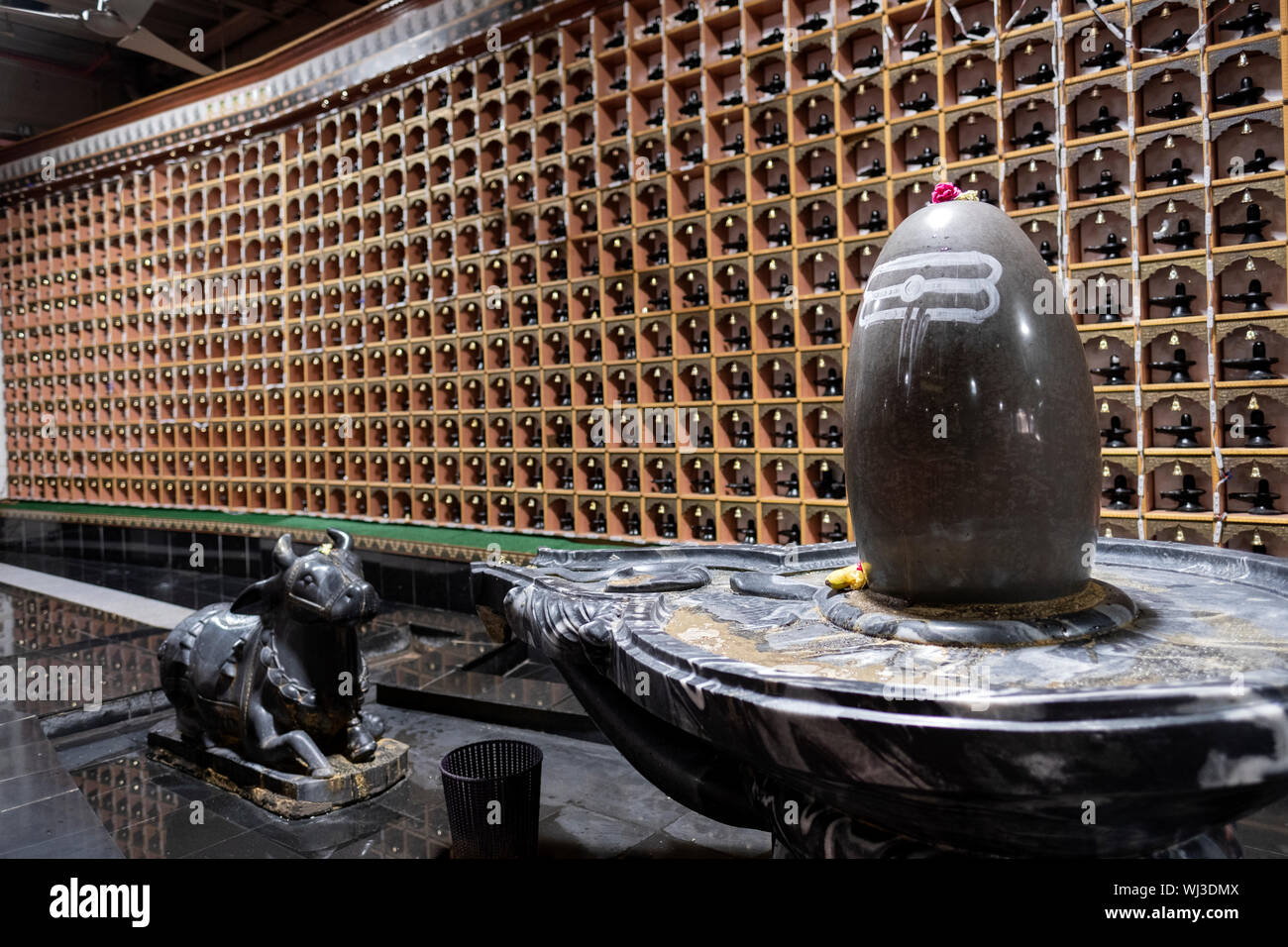 A large sized Shiva LIngam in front of a graphic wall of many miniature lingams. At a Hindu temple in Woodside, Queens, New York City. Stock Photo