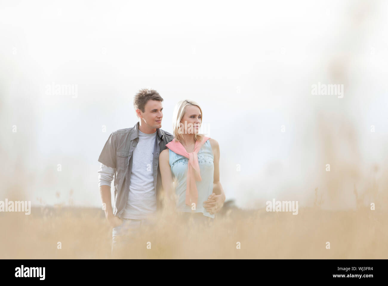 Thoughtful young couple looking away while standing at field Stock Photo