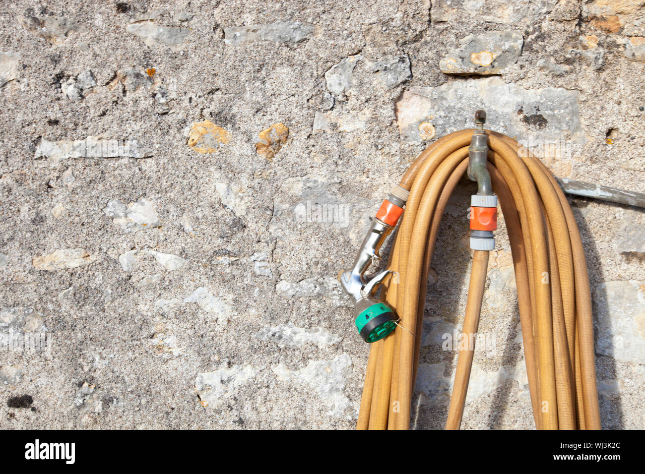 Coiled garden hose hanging on faucet against stone wall Stock Photo Alamy