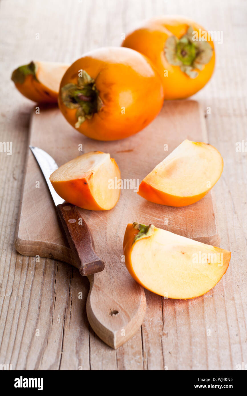 ripe persimmons and knife on wooden board Stock Photo