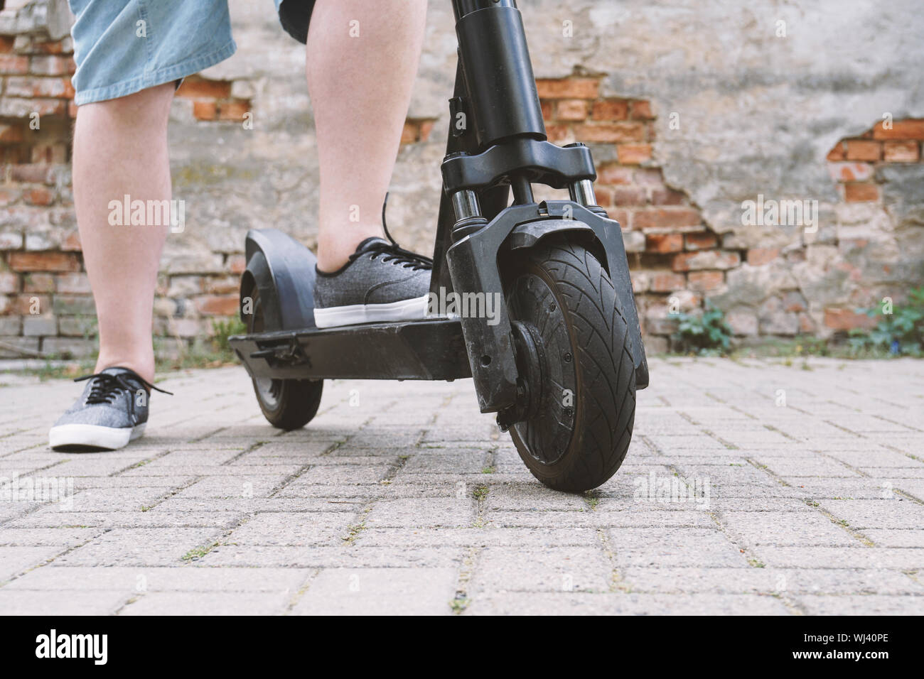 legs of unrecognizable man wearing shorts with electric kick scooter or e-scooter - e-mobility or micro-mobility hipster lifestyle trend Stock Photo