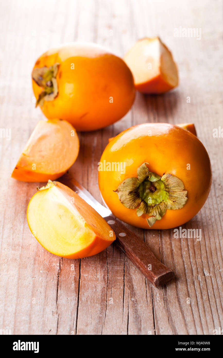 fresh sliced persimmons and knife on wooden background Stock Photo