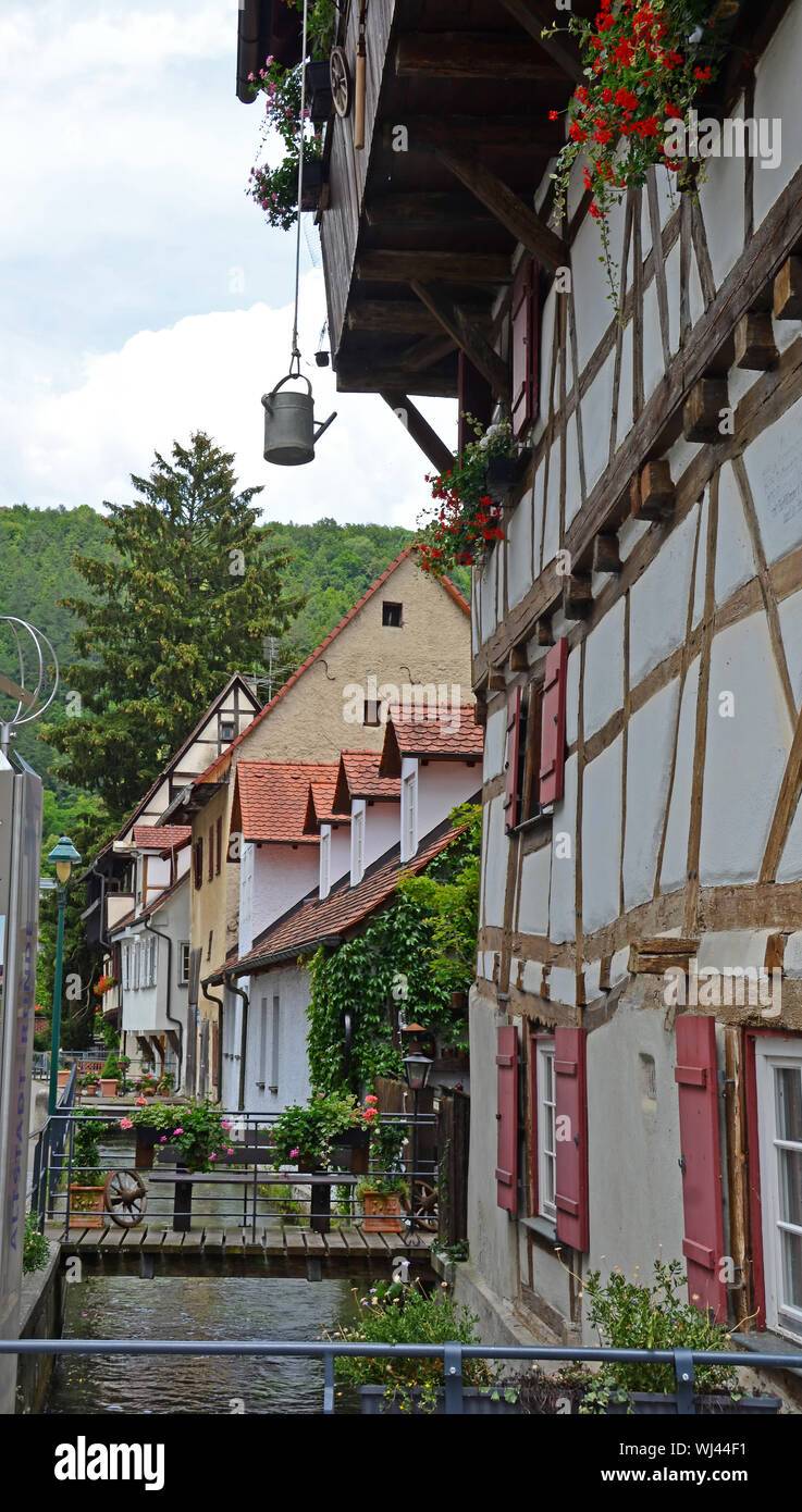 German half timbered building in medieval town built alongside a small canal, in the Swabian Jura region. A watering can provides water for the window Stock Photo